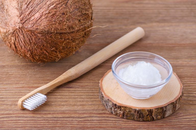 Coconut, a toothbrush, and a bowl with melted coconut oil on a wood table